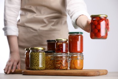 Photo of Woman with jars of different pickled products at table against light background, closeup