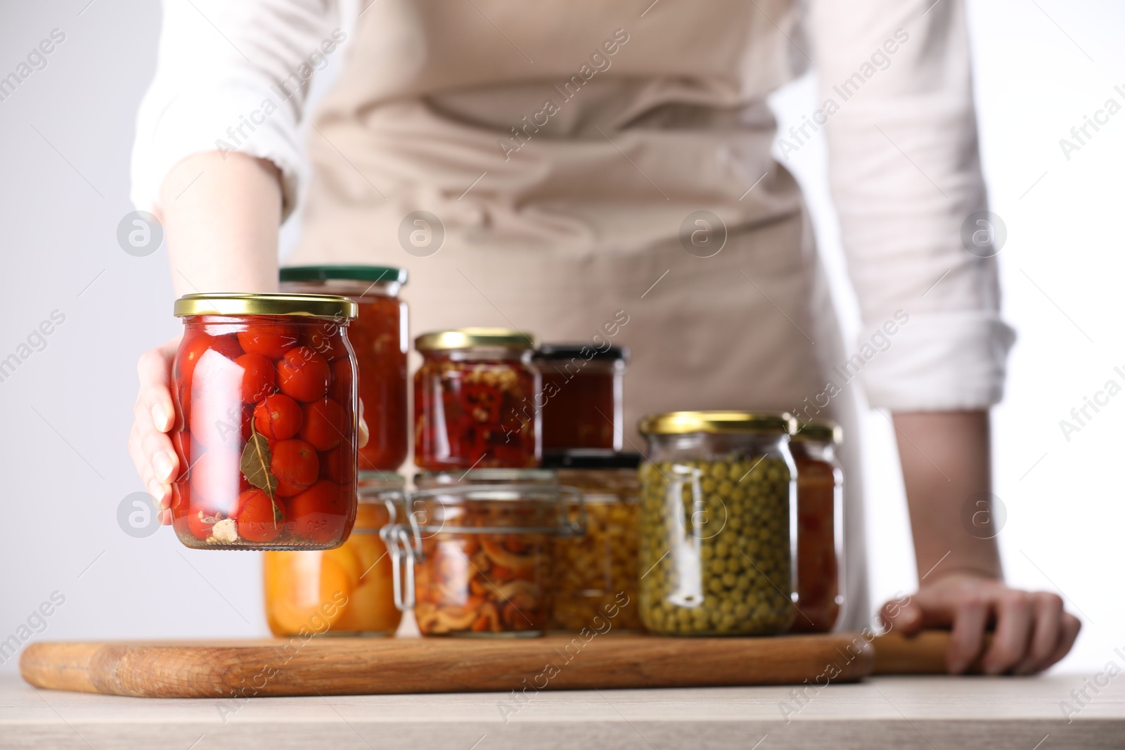 Woman with jars of different pickled products at table against light background, closeup Photo of Woman with jars of different pickled products at table against light background, closeup