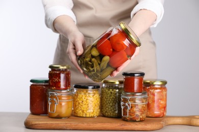 Photo of Woman with jars of different pickled products at table against light grey background, closeup