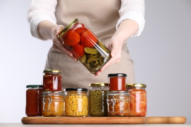 Photo of Woman with jars of different pickled products at table against light grey background, closeup