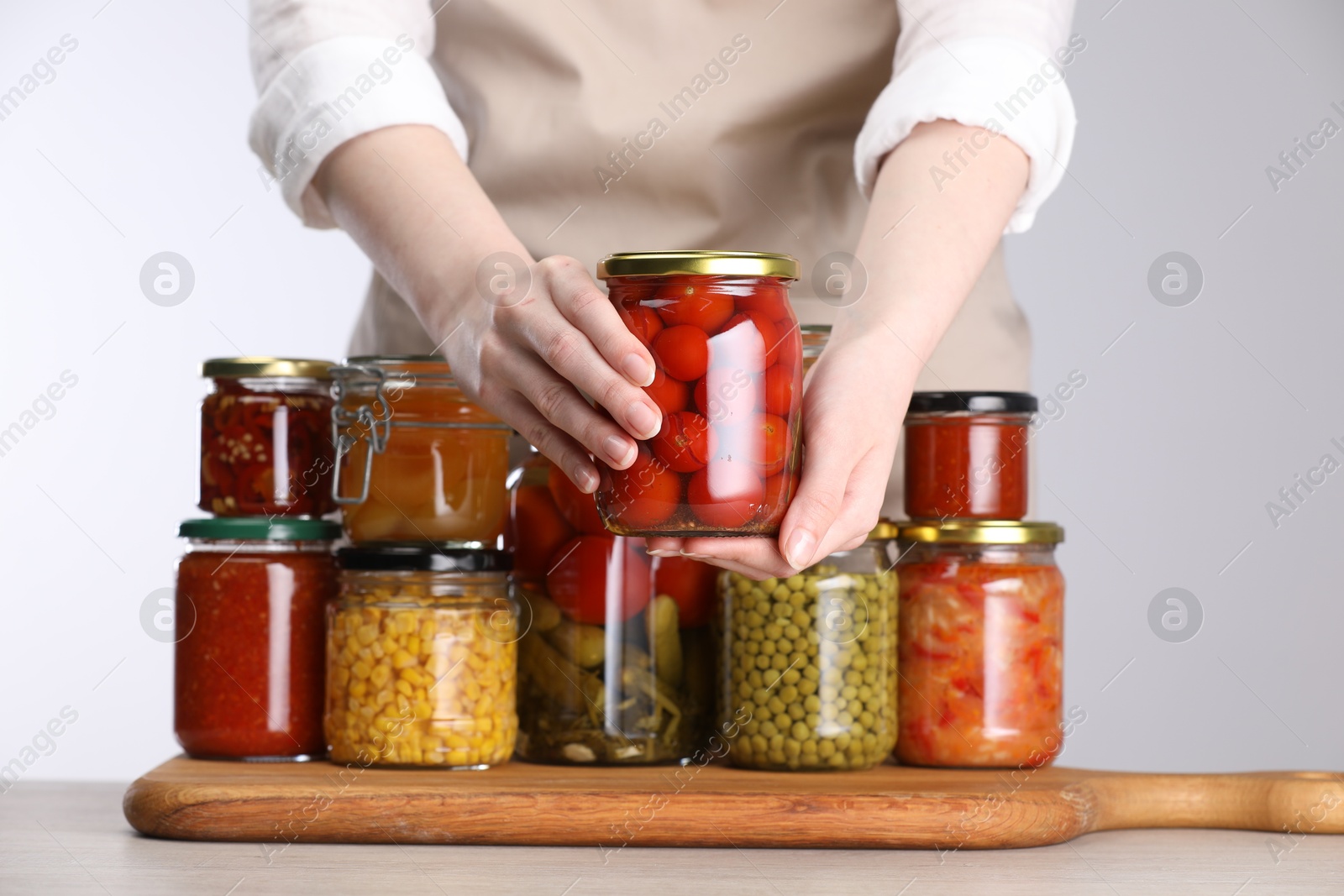 Woman with jars of different pickled products at table against light grey background, closeup Photo of Woman with jars of different pickled products at table against light grey background, closeup