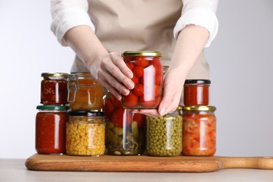 Photo of Woman with jars of different pickled products at table against light grey background, closeup
