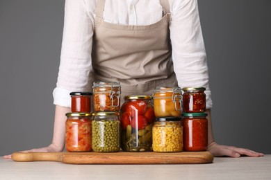 Photo of Woman with jars of different pickled products at table against grey background, closeup