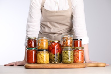Photo of Woman with jars of different pickled products at table against light grey background, closeup