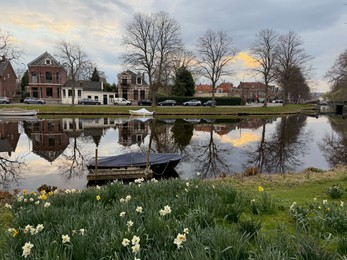 Photo of Leiden, Netherlands - March 22, 2025: Beautiful buildings and trees near city canal with moored boats on cloudy day