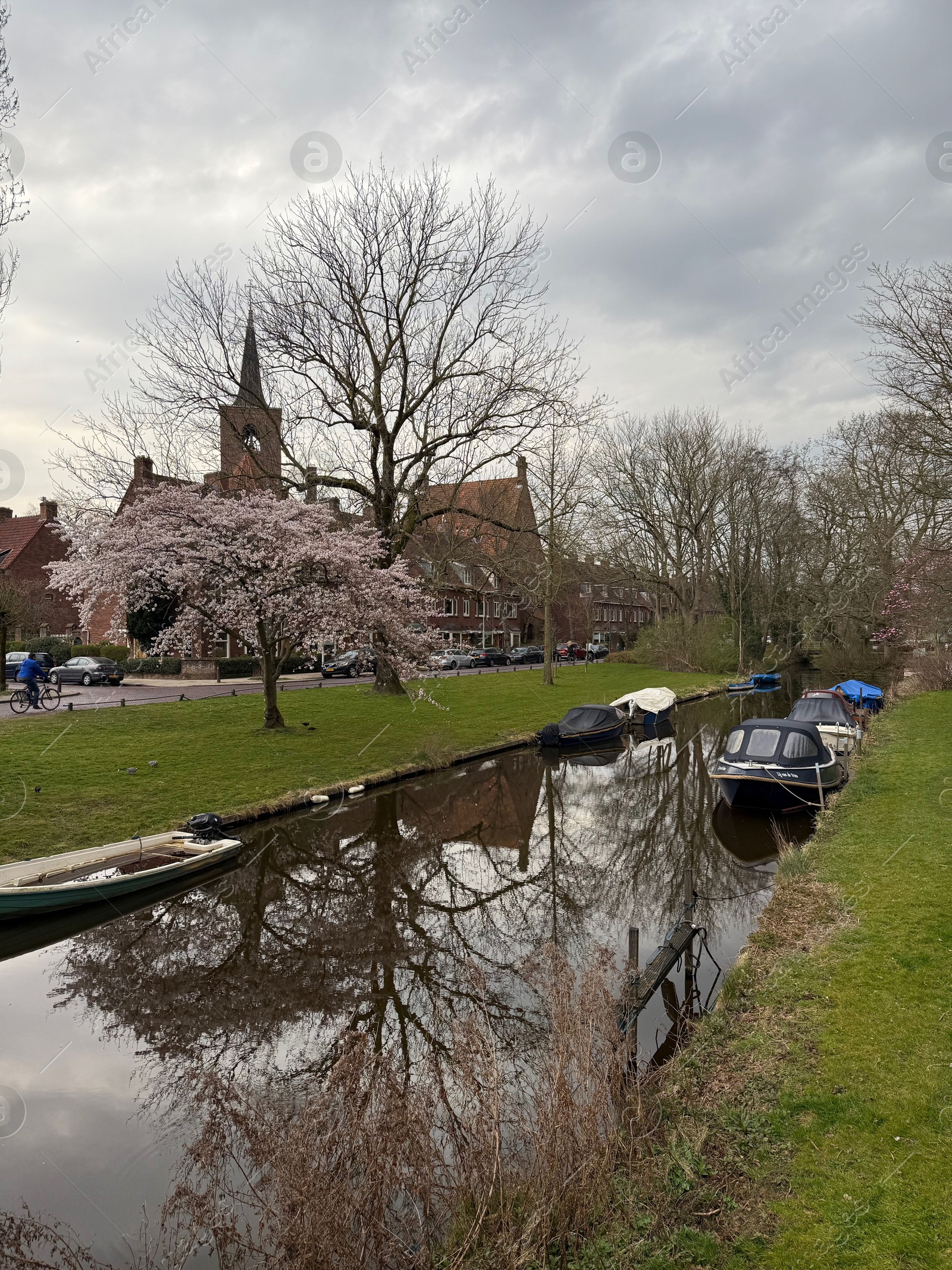 Leiden, Netherlands - March 22, 2025: Beautiful buildings and trees near city canal with moored boats on cloudy day Photo of Leiden, Netherlands - March 22, 2025: Beautiful buildings and trees near city canal with moored boats on cloudy day