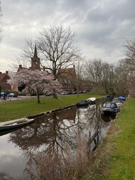 Photo of Leiden, Netherlands - March 22, 2025: Beautiful buildings and trees near city canal with moored boats on cloudy day