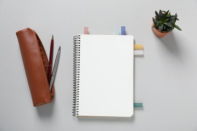 Photo of Open blank notebook with colorful stickers, pens and floral decor on light grey background, flat lay