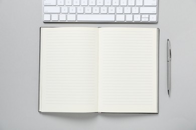 Photo of Open blank notebook, computer keyboard and pen on light grey background, flat lay