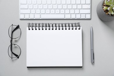 Photo of Open blank notebook, computer keyboard, glasses, pen and floral decor on light grey background, flat lay