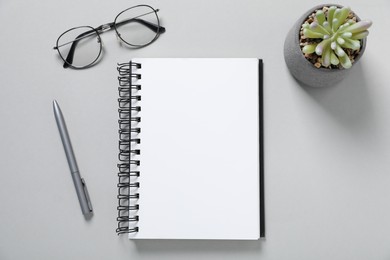 Photo of Open blank notebook, glasses, pen and floral decor on light grey background, flat lay