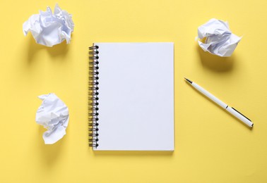 Photo of Open blank notebook, crumpled paper and pen on yellow background, flat lay