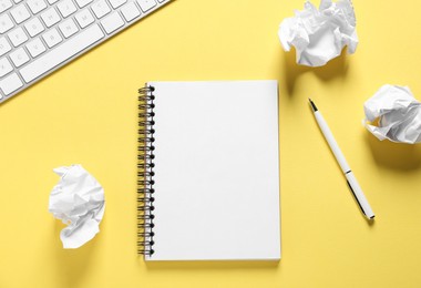 Photo of Open blank notebook, crumpled paper, pen and computer keyboard on yellow background, flat lay