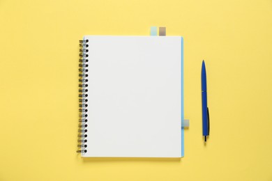 Photo of Open blank notebook and pen on yellow background, flat lay