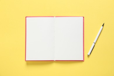 Photo of Open blank notebook and pen on yellow background, flat lay