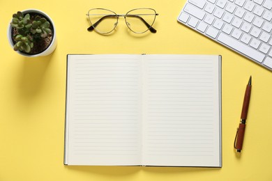 Photo of Open blank notebook, pen, glasses, computer keyboard and floral decor on yellow background, flat lay