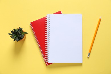 Photo of Open blank notebook, pencil and floral decor on yellow background, flat lay