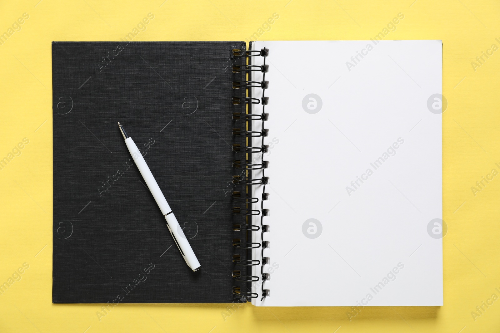 Open blank notebook and pen on yellow background, top view Photo of Open blank notebook and pen on yellow background, top view