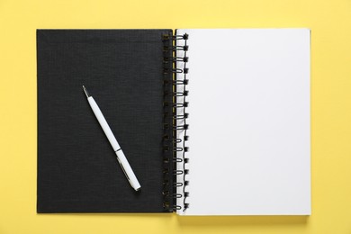 Photo of Open blank notebook and pen on yellow background, top view