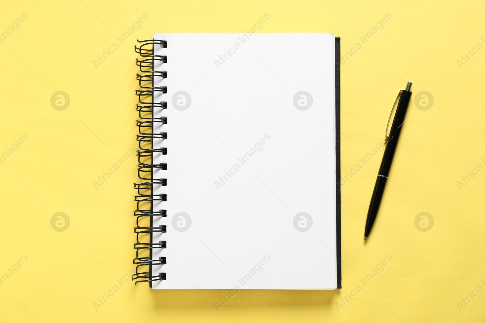 Open blank notebook and pen on yellow background, flat lay Photo of Open blank notebook and pen on yellow background, flat lay