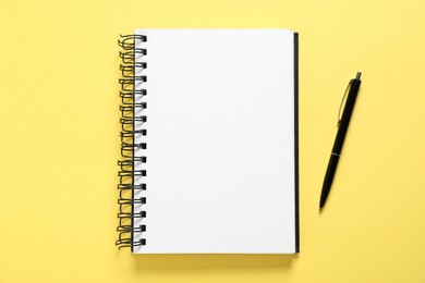 Photo of Open blank notebook and pen on yellow background, flat lay