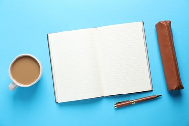 Photo of Open blank notebook, pencil case, pen and coffee on light blue background, flat lay