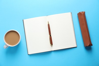 Photo of Open blank notebook, pencil case, pen and coffee on light blue background, flat lay