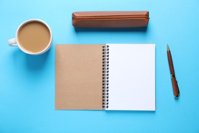 Photo of Open blank notebook, pencil case, pen and coffee on light blue background, flat lay