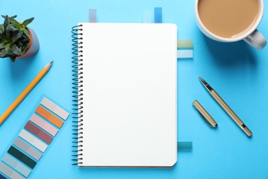 Photo of Open blank notebook, other stationery, coffee and floral decor on light blue background, flat lay