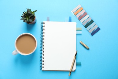 Photo of Open blank notebook, other stationery, coffee and floral decor on light blue background, flat lay