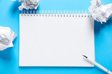 Photo of Open blank notebook, crumpled paper and pen on light blue background, flat lay