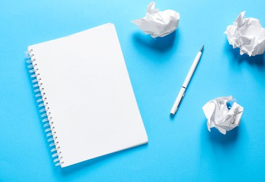 Photo of Open blank notebook, crumpled paper and pen on light blue background, flat lay