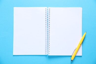 Photo of Open blank notebook and pen on light blue background, top view