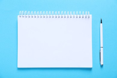 Photo of Open blank notebook and pen on light blue background, flat lay