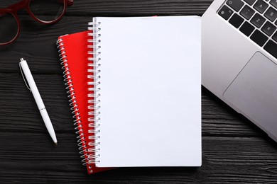 Photo of Open blank notebook, pen, laptop and glasses on black wooden table, flat lay