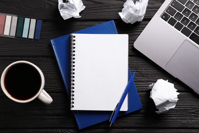 Photo of Open blank notebook, other stationery, coffee, crumpled paper and laptop on black wooden table, flat lay