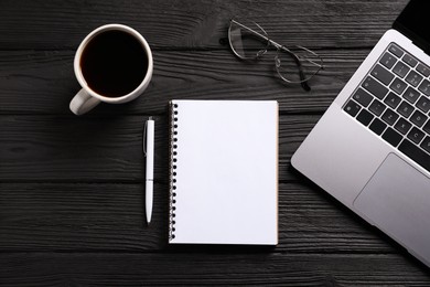 Photo of Open blank notebook, pen, coffee, laptop and glasses on black wooden table, flat lay