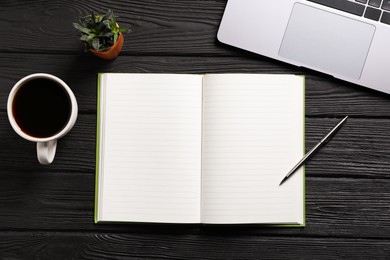 Photo of Open blank notebook, pen, coffee, laptop and floral decor on black wooden table, flat lay