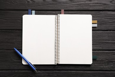 Photo of Open blank notebook with colorful stickers and pen on black wooden table, top view