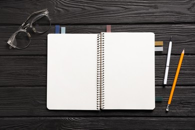 Photo of Open blank notebook with colorful stickers, pen, pencil and glasses on black wooden table, flat lay