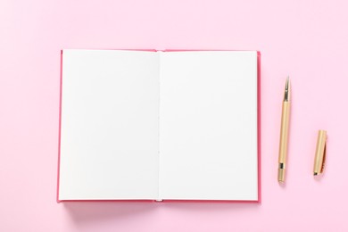 Photo of Open blank notebook and pen on pink background, flat lay