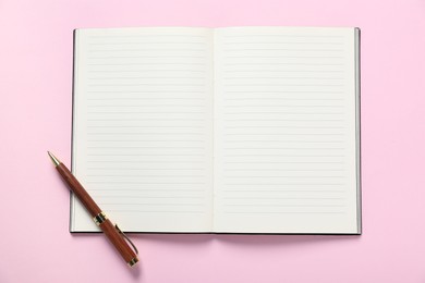 Photo of Open blank notebook and pen on pink background, top view