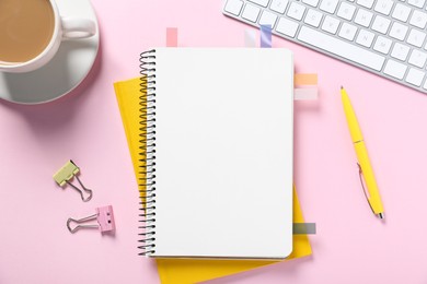 Photo of Open blank notebook with colorful stickers, other stationery, coffee and computer keyboard on pink background, flat lay