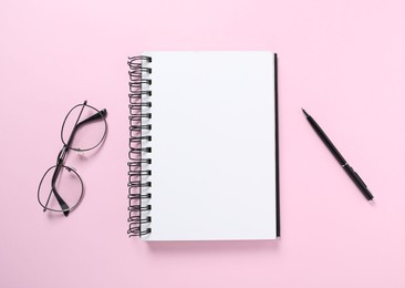 Photo of Open blank notebook, glasses and pen on pink background, flat lay