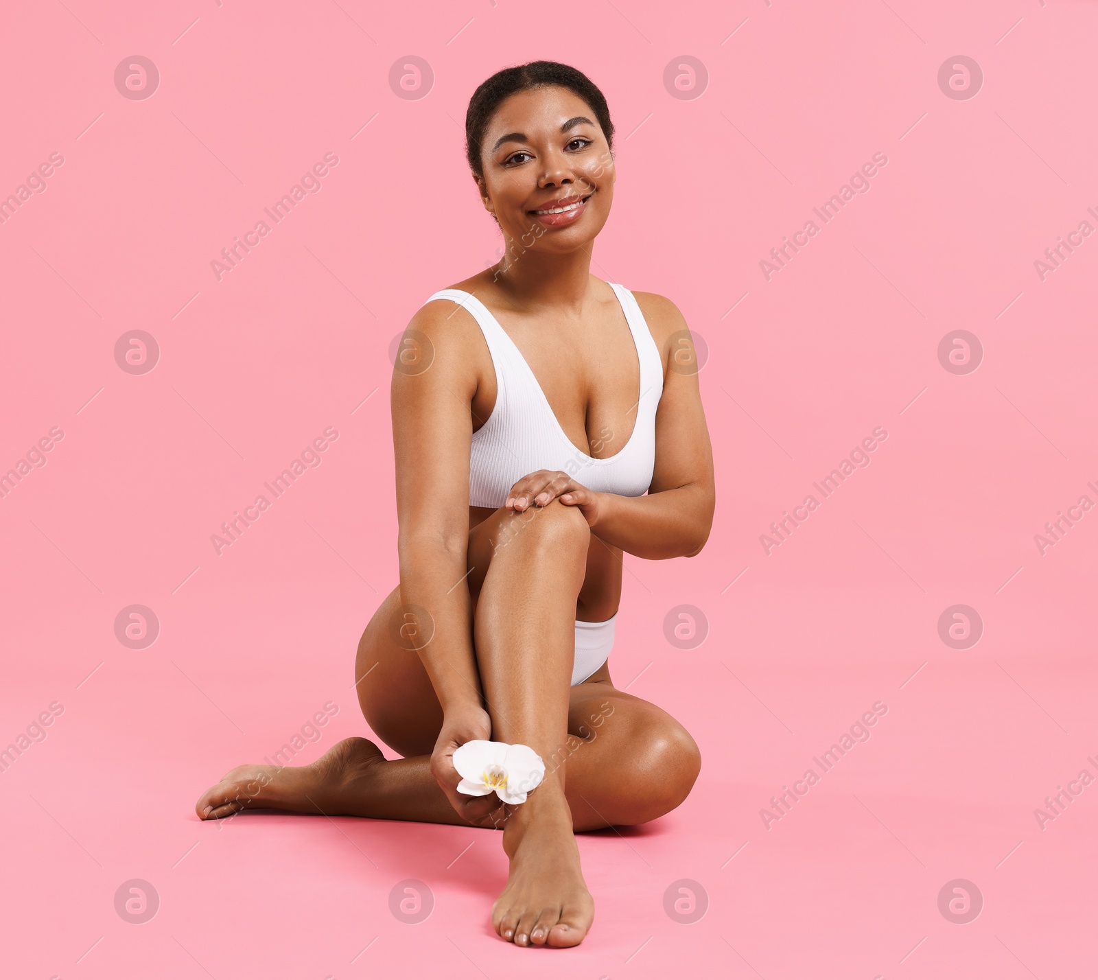 Woman in underwear with flower showing smooth skin after epilation procedure on pink background Photo of Woman in underwear with flower showing smooth skin after epilation procedure on pink background