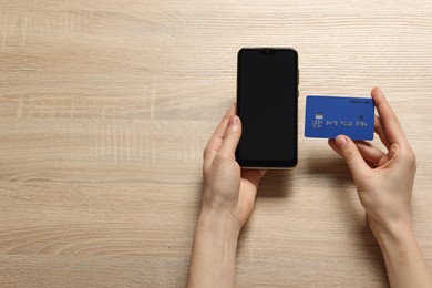 Photo of Woman with credit card and smartphone paying online at wooden table, top view. Space for text
