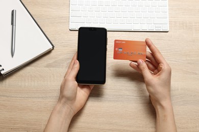 Photo of Woman with credit card and smartphone paying online at wooden table, top view