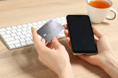 Photo of Woman with credit card and smartphone paying online at wooden table, closeup