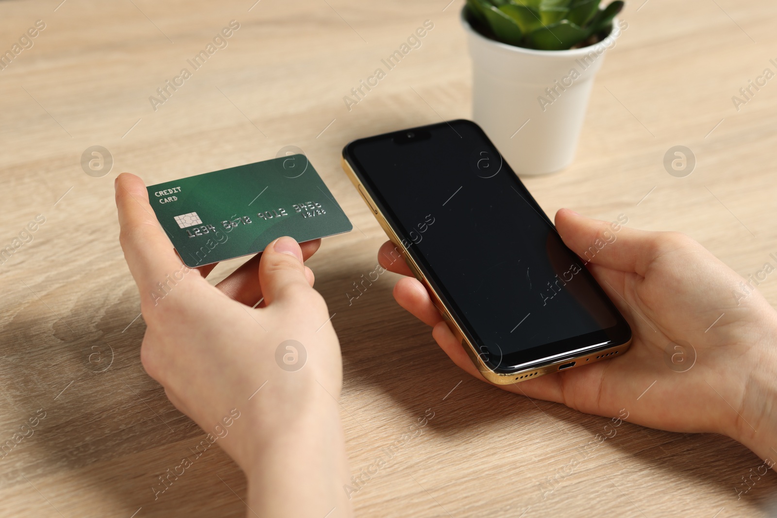 Photo of Woman with credit card and smartphone paying online at wooden table, closeup