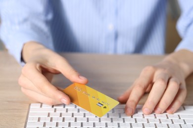 Photo of Online payment. Woman with credit card typing on computer keyboard at wooden table, closeup